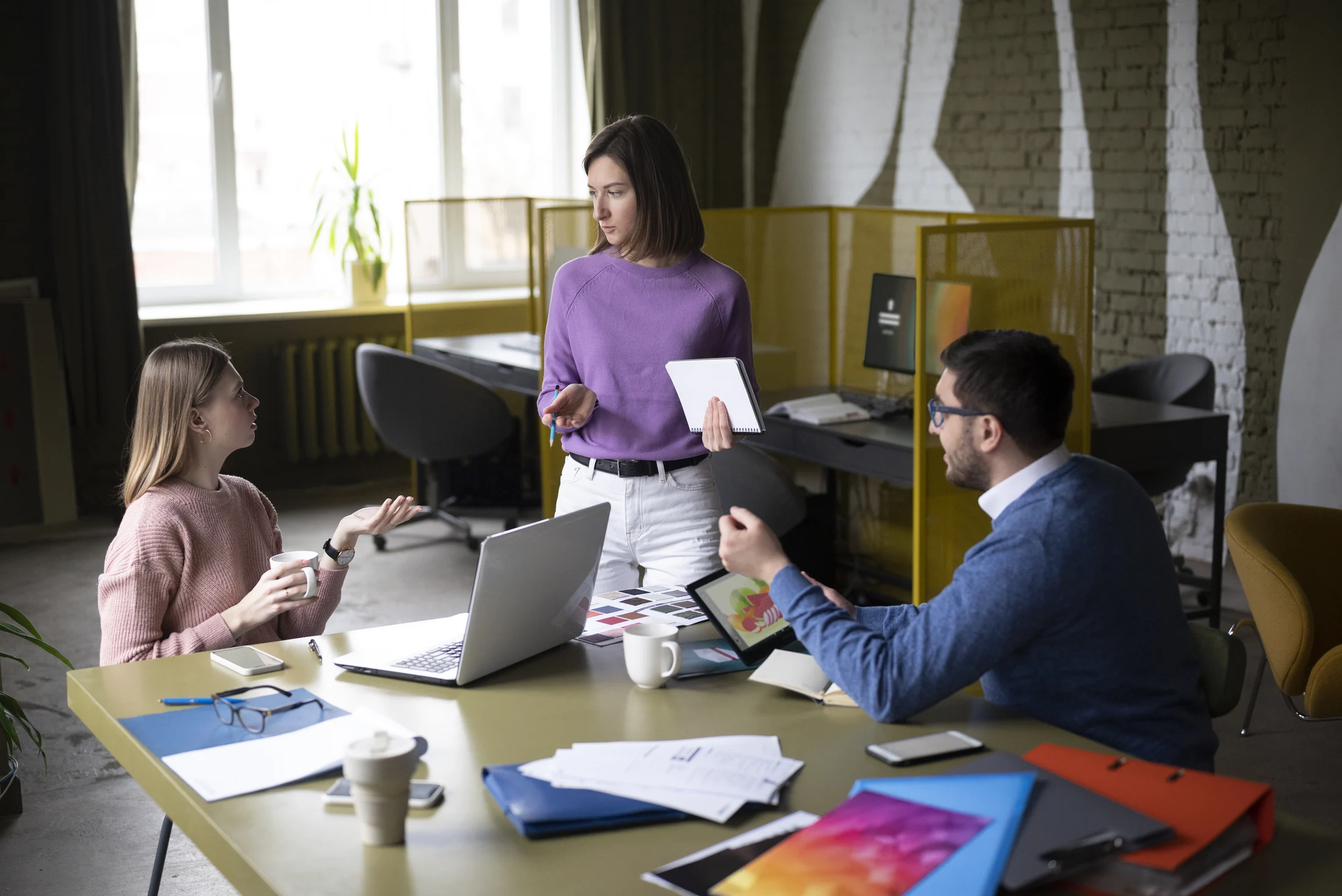 Illustrative stock photograph of three colleagues discussing work around a laptop and documents.
