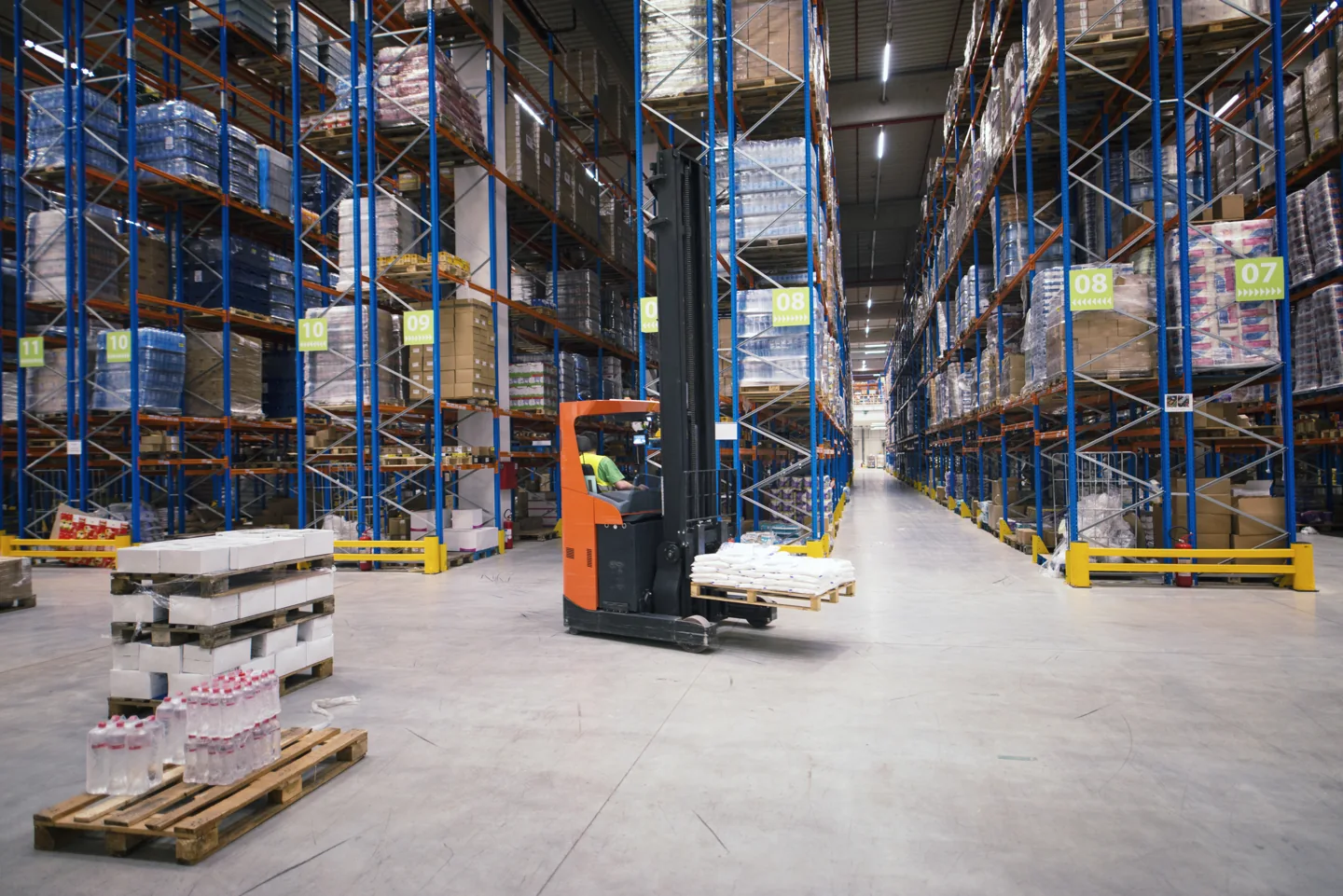 Stock photograph of tall warehouse racks and a powered pallet truck in a storage aisle