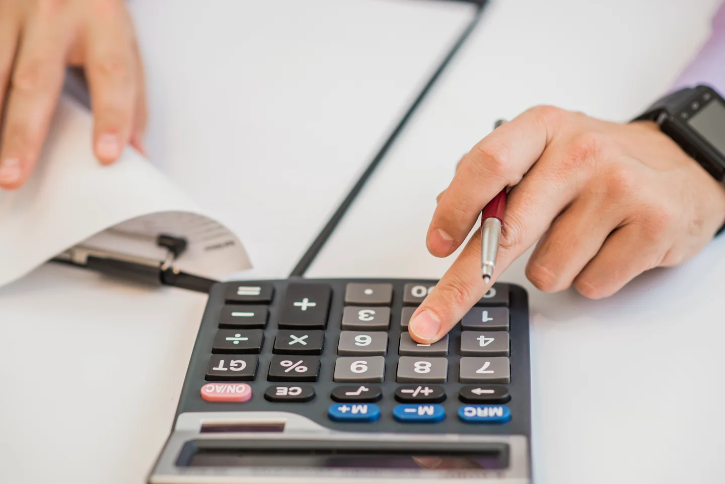 Stock photograph of hands checking paperwork with a calculator and pen
