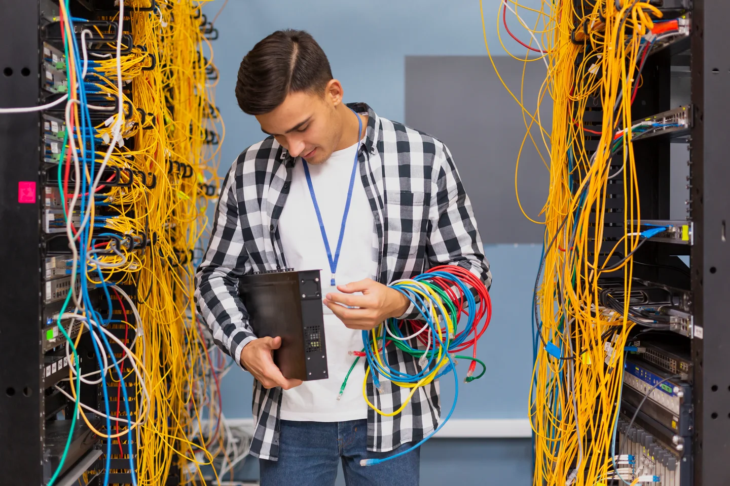 Stock photograph of a network technician handling a switch and cables between equipment racks