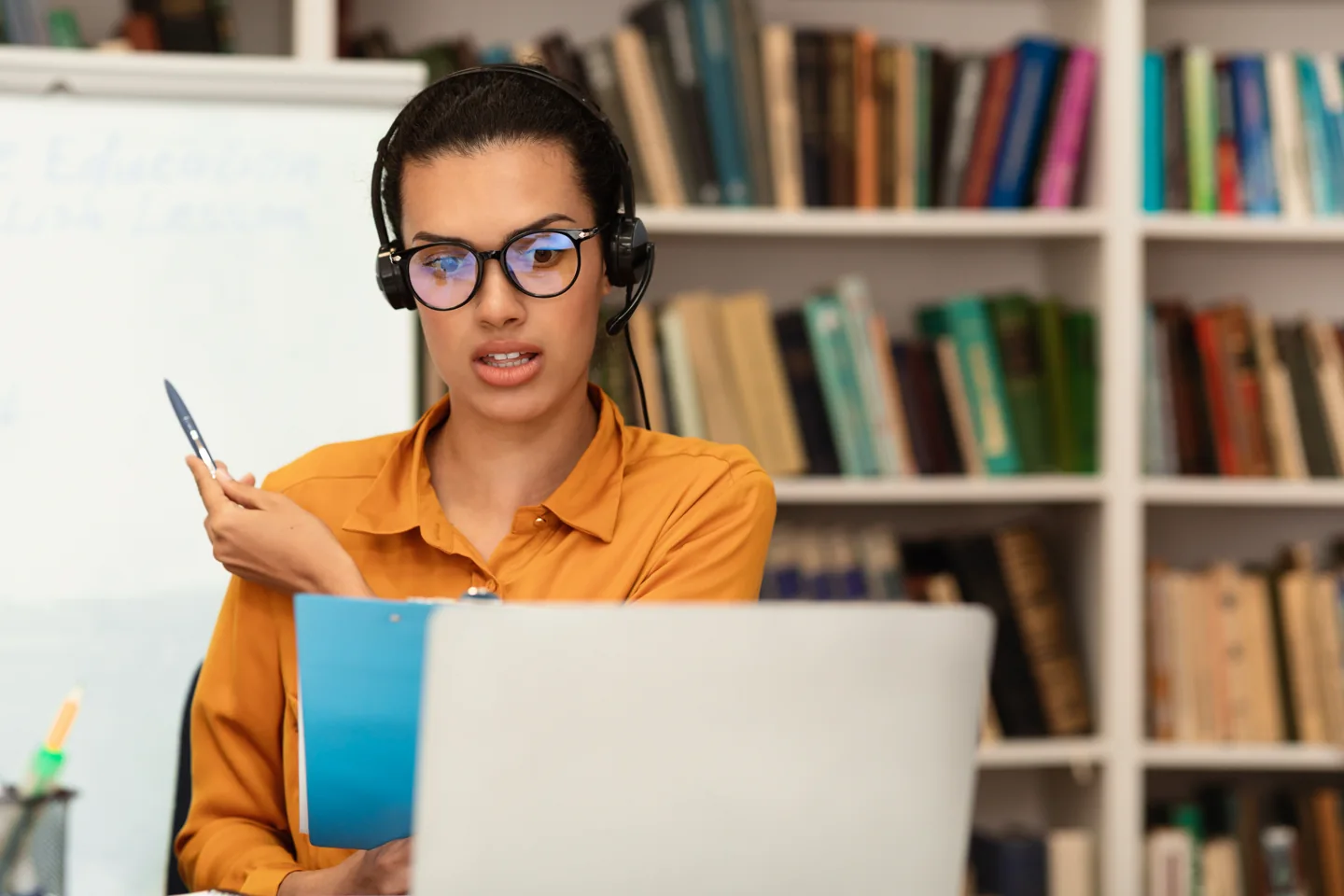 Stock photograph of a teacher wearing a headset and speaking toward a laptop beside a whiteboard