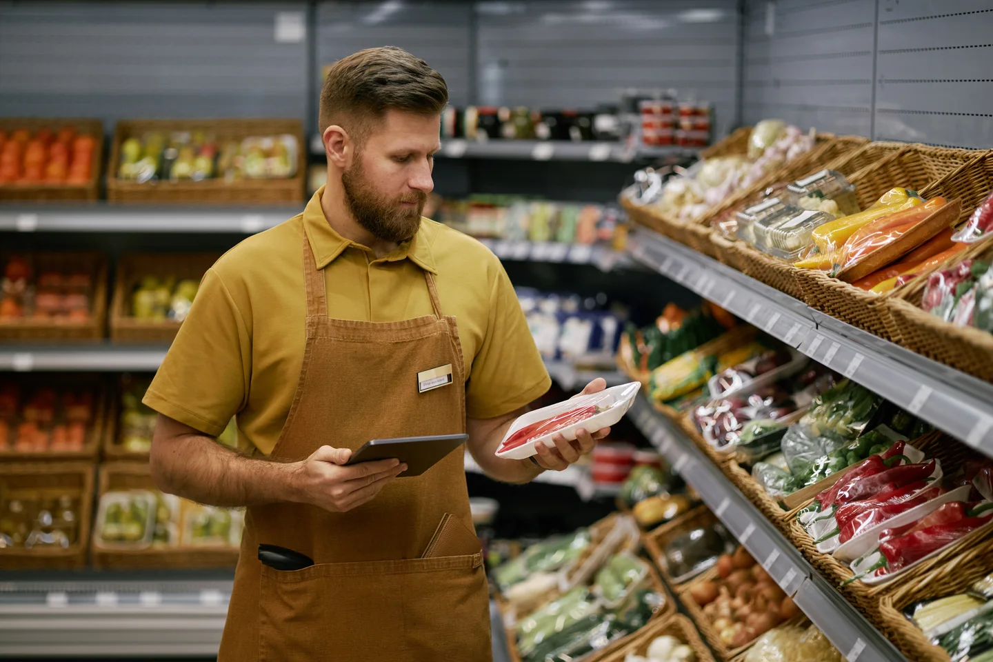 Stock photograph of a grocery worker checking a packaged product beside stocked shelves